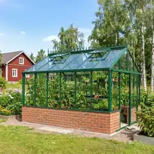 Vihreä kasvihuone tiilestä tehdyllä alaosalla, puutarhassa